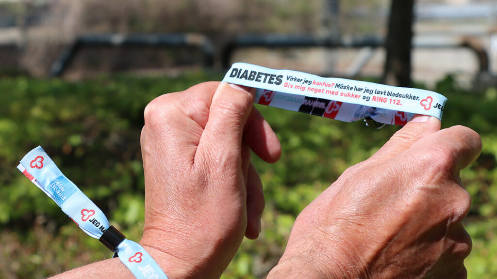 Lyseblåt festivalarmbånd fra Diabetesforeningen. Et armbånd sidder på et håndled, og et andet holdes frem, så teksten "Jeg har diabetes" kan ses.