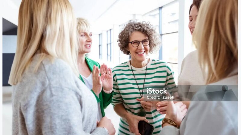 På billedet ser man 4 mennesker stå i en gruppe og have en dialog - de smiler og er glade